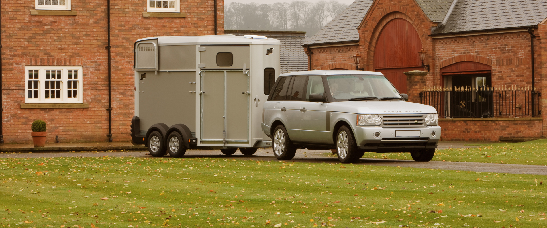 A car towing a horse trailer out of a yard