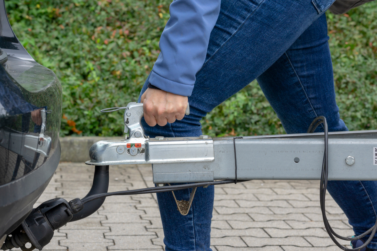 A person hitching a trailer to a car's tow bar