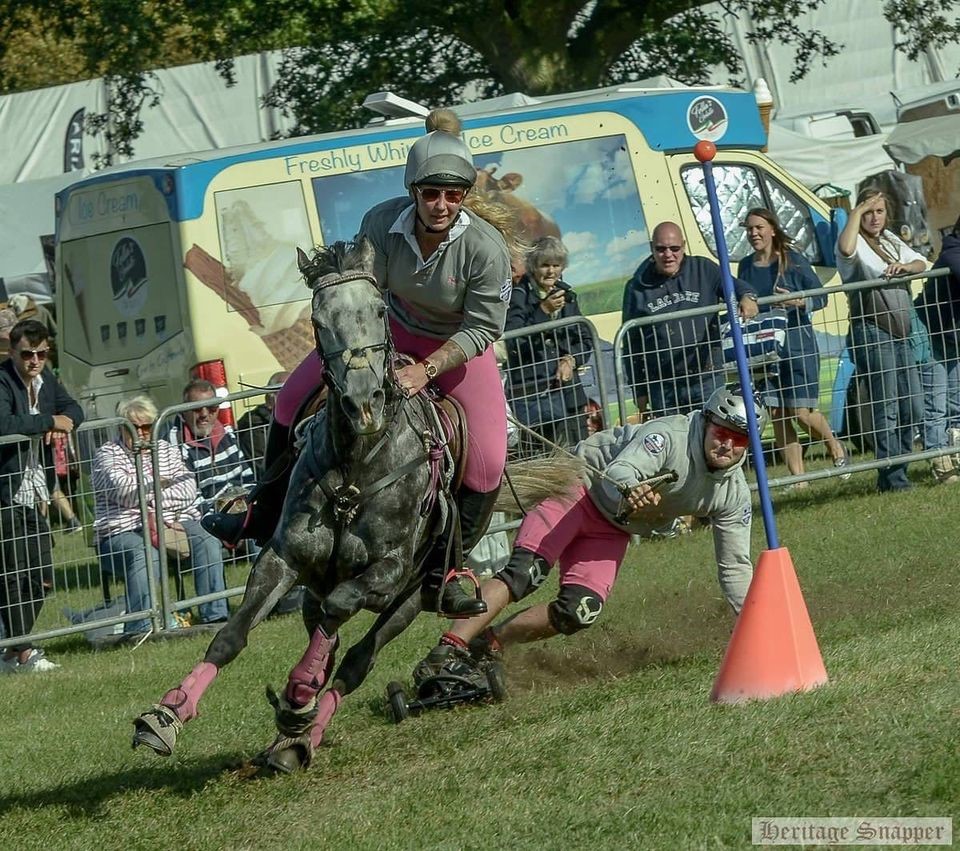 A horse and rider pulling a person riding a horse board on a rope around a course at a country fair