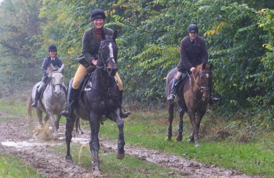 Three horse and riders trotting along a muddy trail in the rain