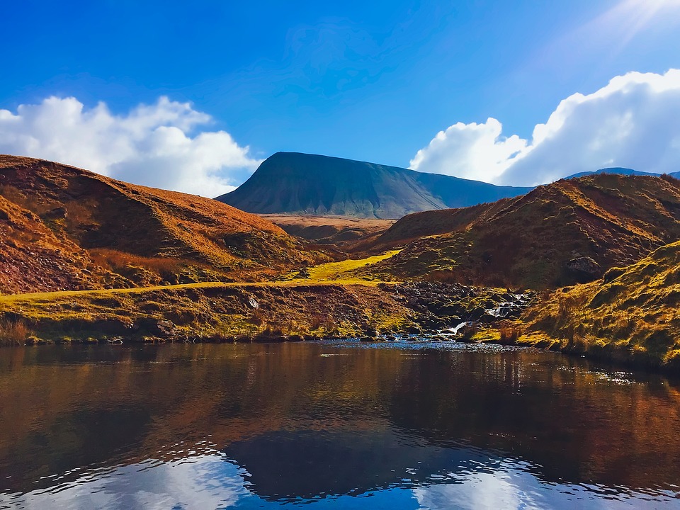 A view across a lake in the Brecon Beacons national park with green hills behind